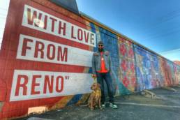 Man standing with dog in front of a graffiti wall.