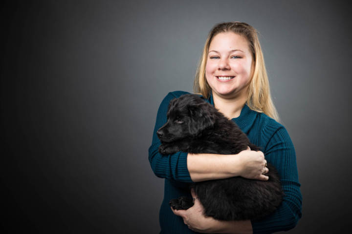 Jaimie Cummings holding a fuzzy black puppy against grey background.
