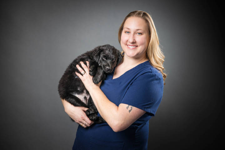 Karrie Wirth holding a fluffy black puppy against grey background.