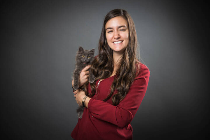 Nayla Garcia holding a fluffy grey kitten against a grey background.