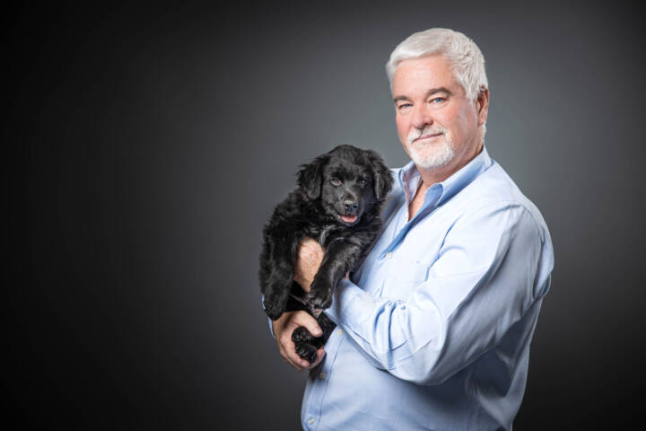 Sean Farnan holding a fluffy black puppy against a grey background.