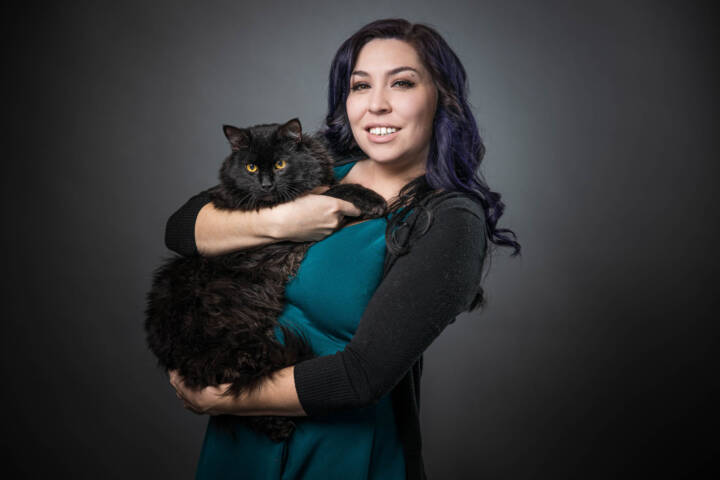 Tara David holding a fluffy black cat against a grey background