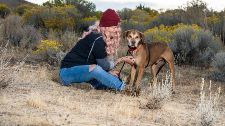 Volunteer in beanie sitting in a desert region with an adoptable dog.