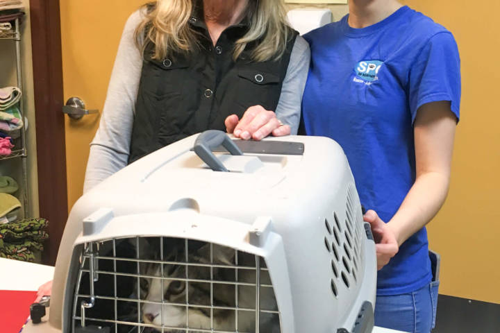 Photo of Cathy and Alyssa standing next to a cat inside a crate, smiling.
